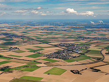 Luftaufnahme Felder mit Siedlungen und Windrädern
